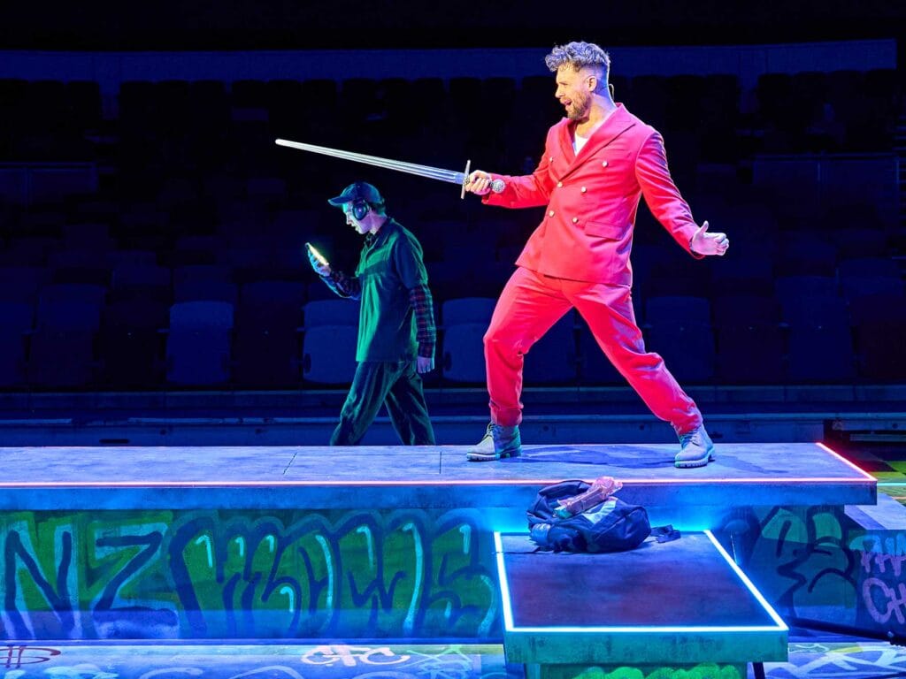 Danny Hatchard as Hugo Bang holding a sword in Top Gs Like Me at Royal & Derngate.